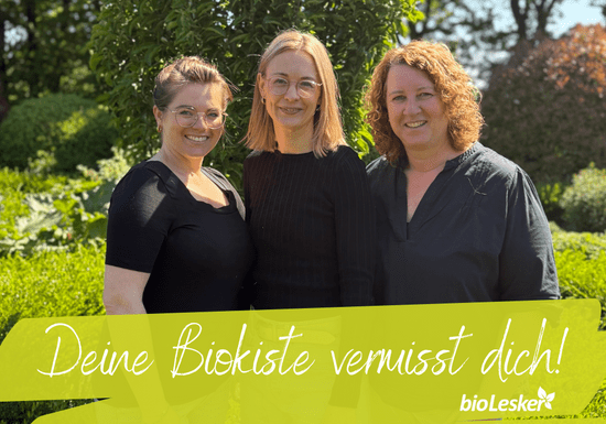 KI generiert: Ein Mann hält ein Huhn in den Armen und trägt ein T-Shirt mit dem Aufdruck "bioLesker". Im Bild steht der Text "Ihre Bio-Kiste vermisst Sie!" vor einem ländlichen Hintergrund.