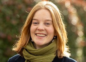 KI generiert: Ein Frau mit rotem Haar lächelt, umgeben von einem verschwommenen grünen Hintergrund.