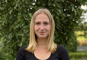 KI generiert: Eine Frau steht vor einem grünen, bewachsenen Hintergrund.