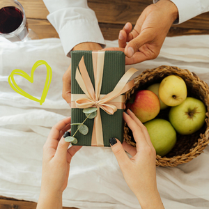 KI generiert: Das Bild zeigt ein in braunes Papier eingewickeltes Geschenk mit einer roten Schnur und einem weißen Herzanhänger. Links oben steht der Text "Geschenkgutscheine".