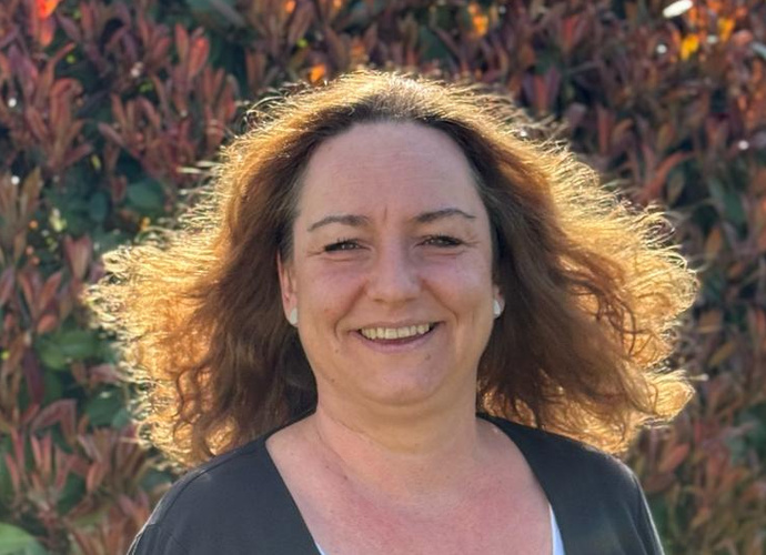 KI generiert: Eine Frau lächelt in die Kamera, Hintergrund ist eine Hecke bei Sonnenlicht.