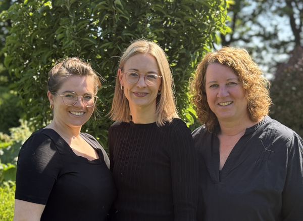 KI generiert: Drei Personen stehen lächelnd in einem sonnigen Garten.