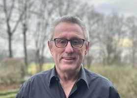 KI generiert: Porträt eines Mannes mit Brille vor unscharfem Hintergrund mit Bäumen.