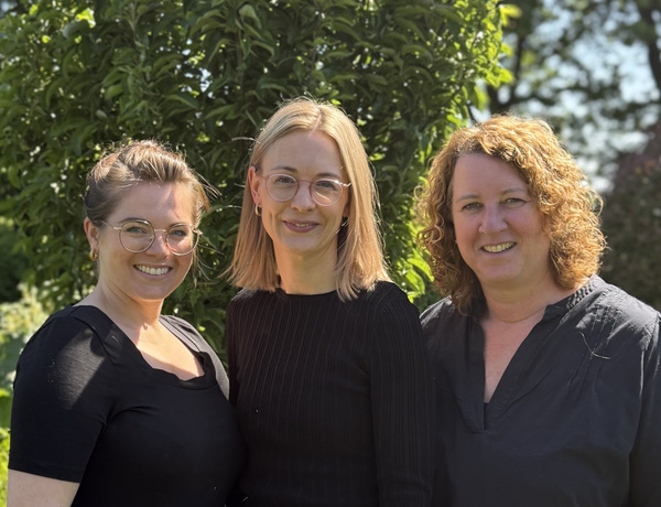 KI generiert: Drei Personen stehen lächelnd vor einem grünen Hintergrund im Freien.