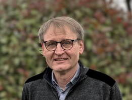 KI generiert: Ein Mann mit Brille im Freien vor unscharfem Hintergrund.