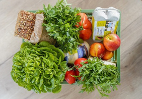 KI generiert: Eine Kiste mit frischem Gemüse, Obst, Eiern und Brot.