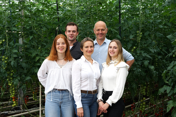 KI generiert: Fünf Personen lächeln in einem Gewächshaus mit Tomatenpflanzen im Hintergrund.