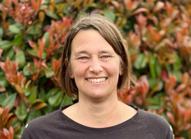 KI generiert: Eine Person lächelt vor einem Hintergrund aus grünen und rötlichen Pflanzen.