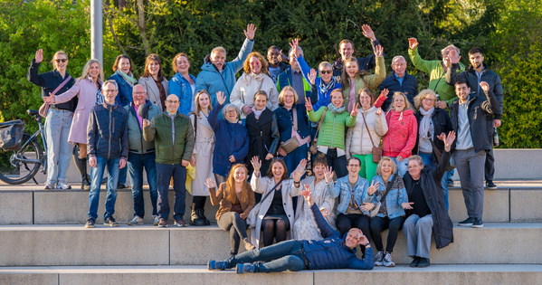 KI generiert: Eine Gruppe Menschen posiert und winkt auf einer Treppe in sonniger Umgebung.