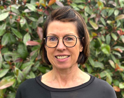 KI generiert: Eine lächelnde Person mit Brille vor einem Hintergrund von grünen Blättern.